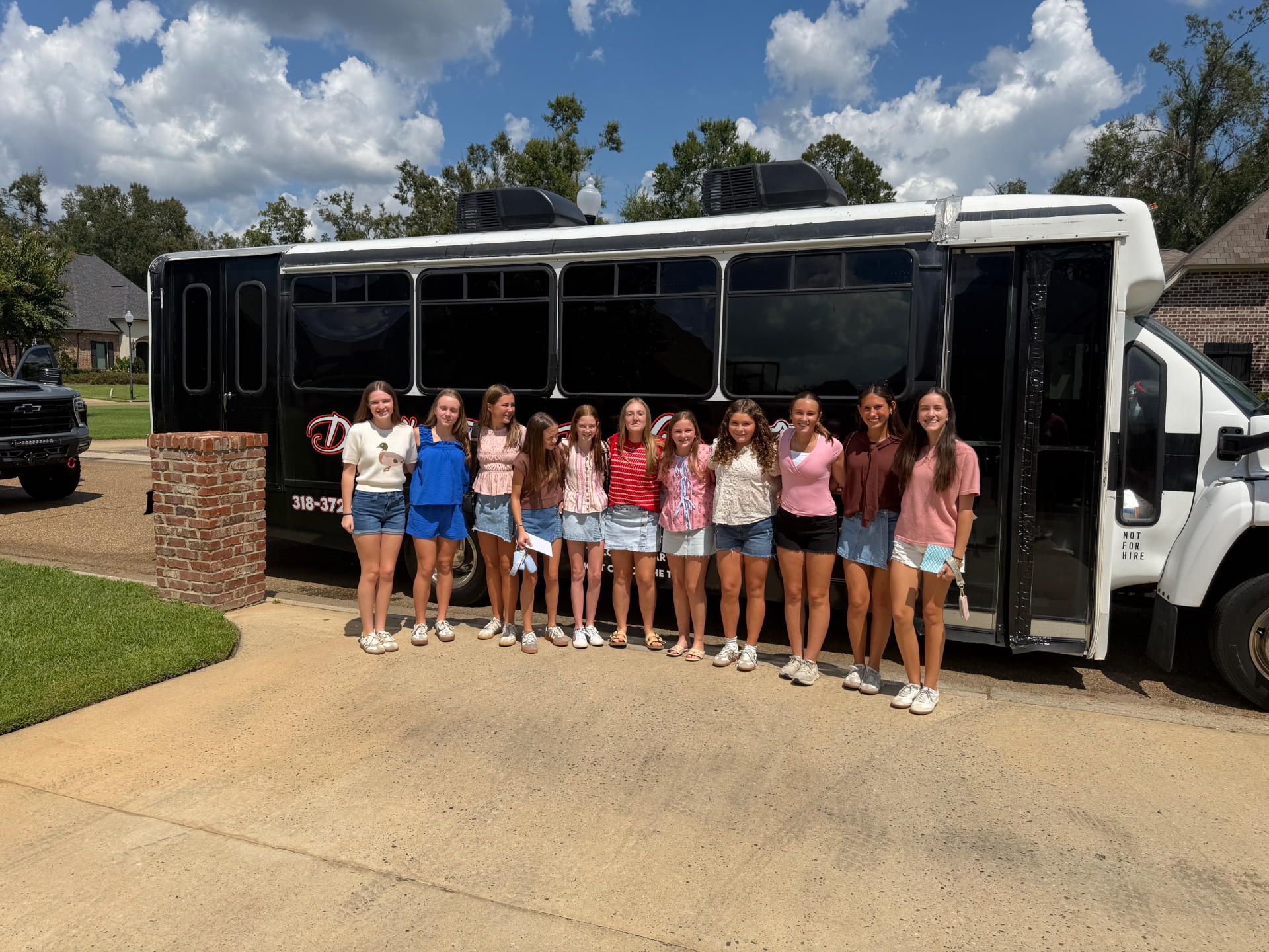 Group of girls celebrating a 14th birthday party beside the black David's Transportation Services party bus